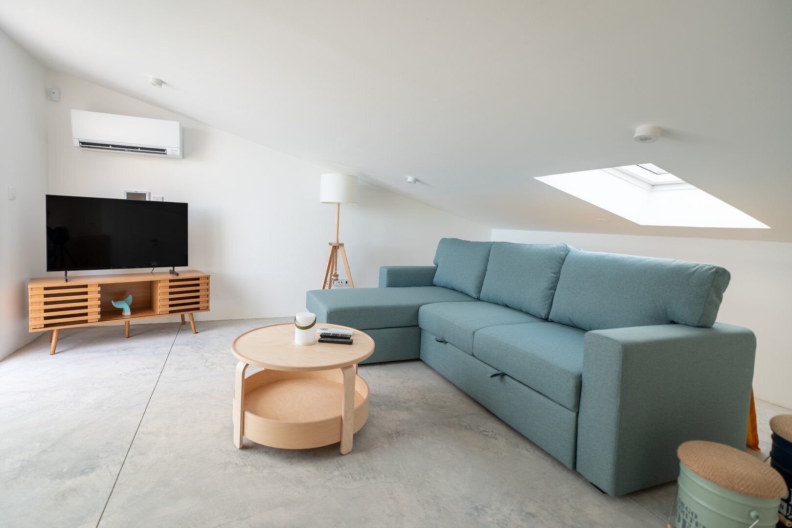 A modern living room with a sectional sofa, a flat-screen TV, a wooden TV stand, a round coffee table, and a skylight.