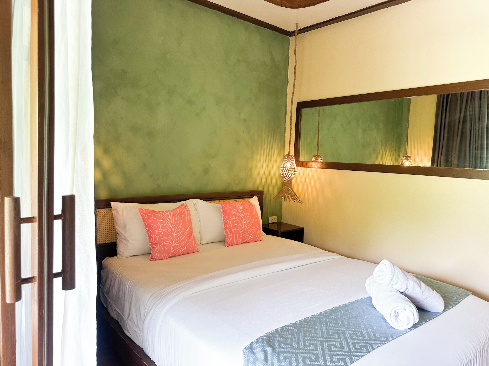 A hotel room with a bed, pillows, a bedside lamp, and a mirror.