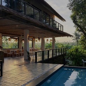 A modern outdoor dining area with a pool, surrounded by lush greenery and large windows. - Jungle Nest Resort (General Luna)