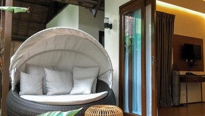 Una stanza con una grande zona salotto rotonda e imbottita di bianco, un tetto di paglia, una scrivania in legno con un televisore e un'ampia finestra con tende.