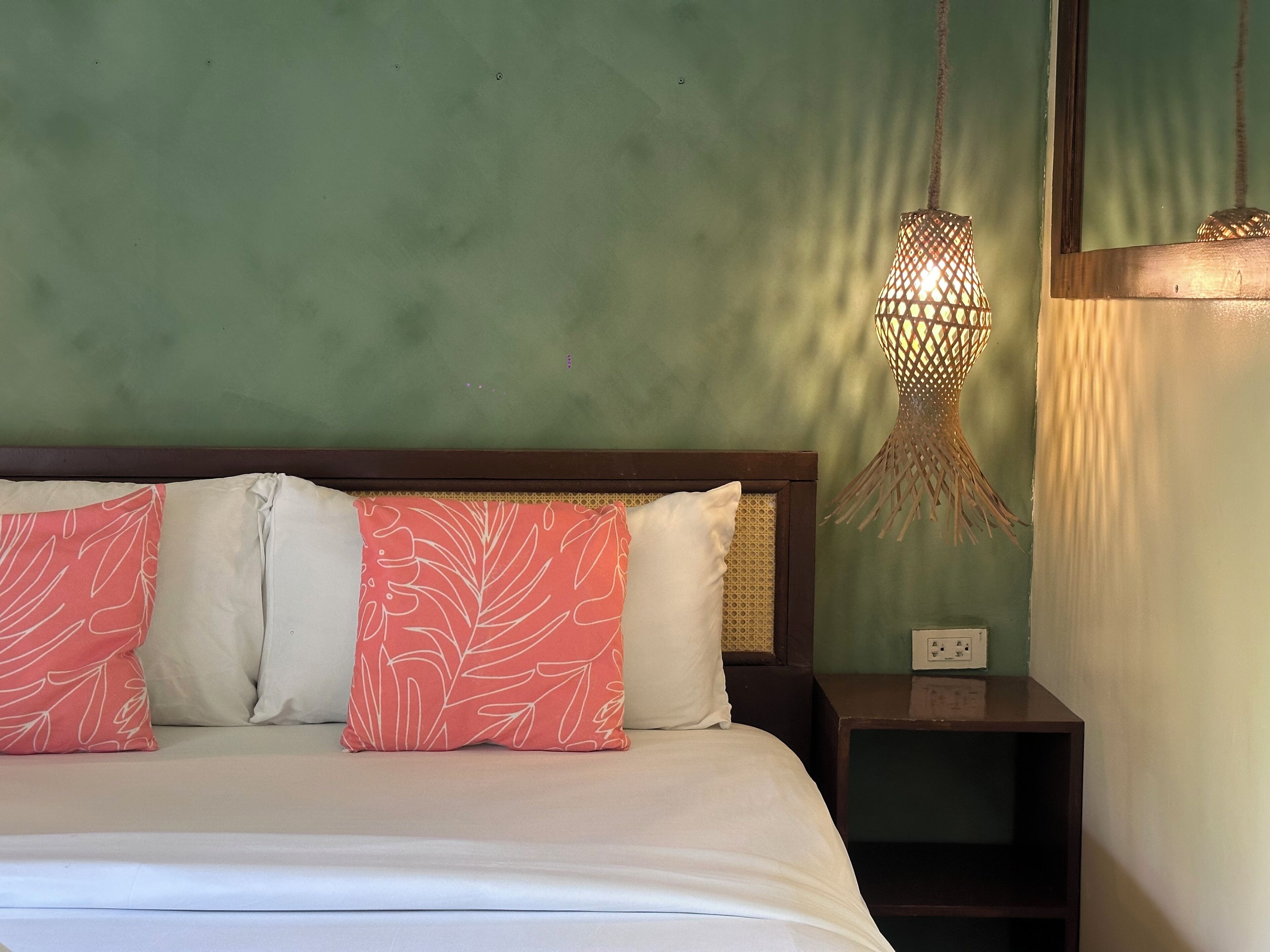 A bed with white and pink patterned pillows, a wooden headboard, and a nightstand with a lamp.