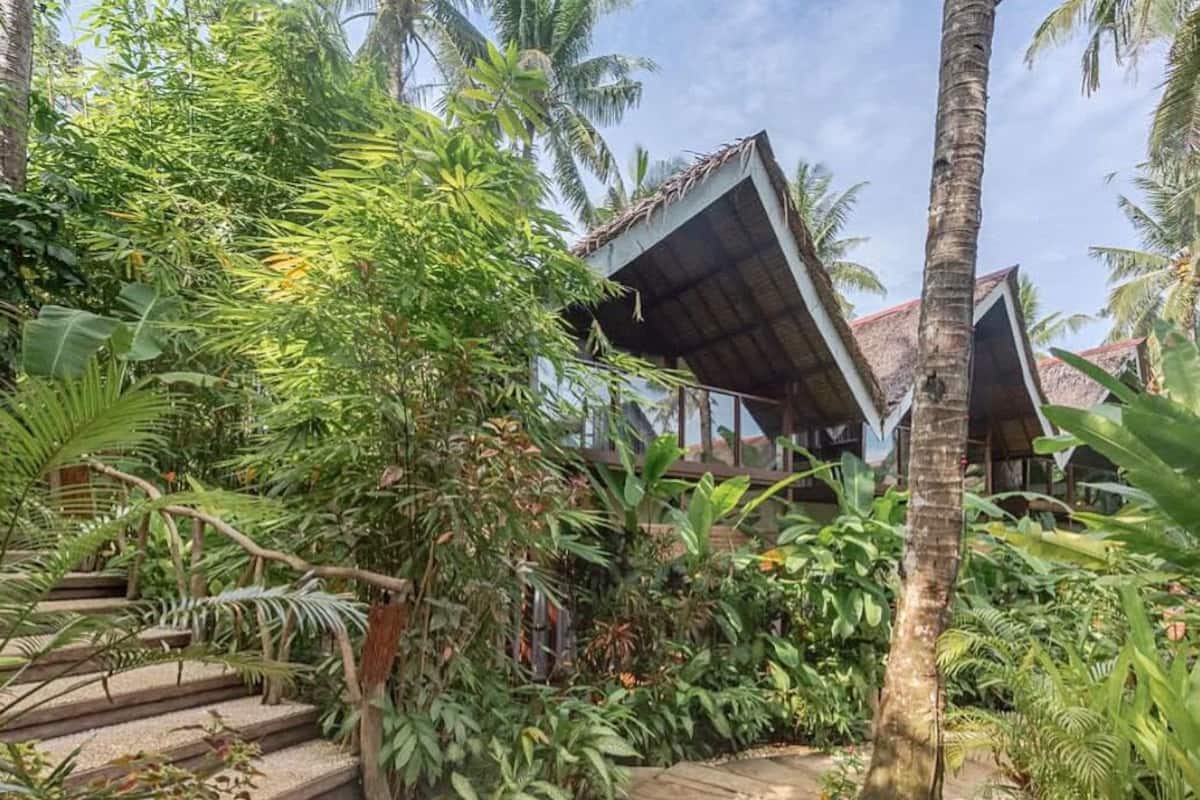 A tropical resort with a thatched-roof structure, surrounded by lush greenery and a stone pathway.