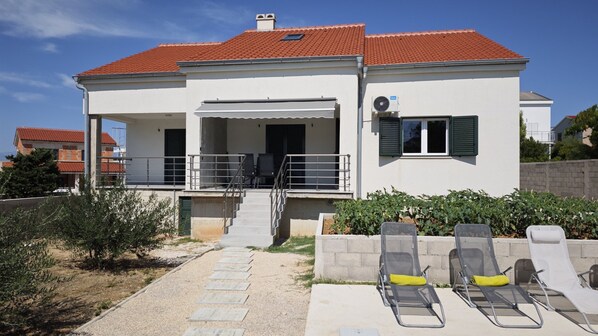 A two-story house with a red-tiled roof, a covered porch with chairs, and a small garden area with a bench. - Beautiful Villa Pauliana (Povljana)