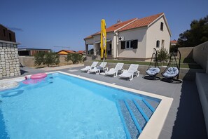 A swimming pool with lounge chairs and a yellow flag, surrounded by a house with a tiled roof. - Beautiful Villa Pauliana (Povljana)