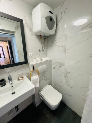 Une salle de bain moderne avec un pare-baignoire en marbre, un lavabo blanc, des toilettes et un bidet portatif.