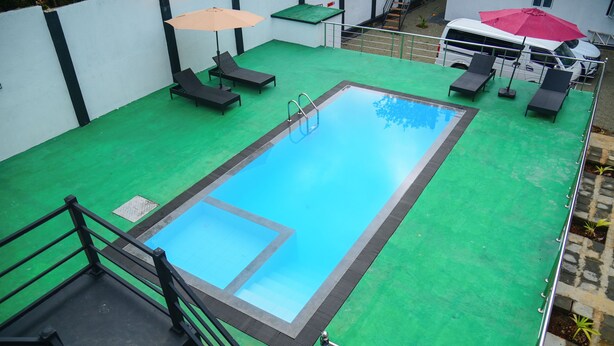 A rooftop swimming pool with a green deck, surrounded by lounge chairs and umbrellas. - Amila Resort (Habarana)