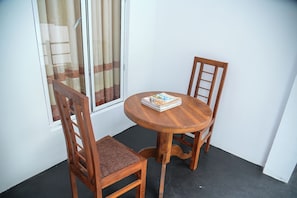 A small wooden table with two chairs, a window with curtains, and a welcome book on the table.