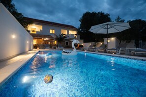 A swimming pool with lounge chairs and umbrellas, surrounded by a building with a balcony. - Holiday Home Lantina With Pool (Novigrad)