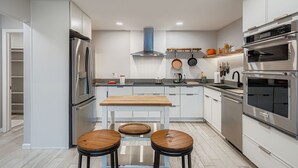 Una cocina moderna con electrodomésticos de acero inoxidable, una isla central con taburetes y armarios blancos.