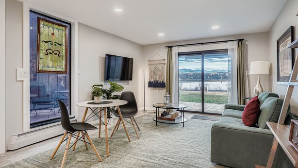 Una sala de estar moderna con un televisor de pantalla plana, una zona de comedor con mesa y sillas, un sofá verde y un ventanal con vistas.