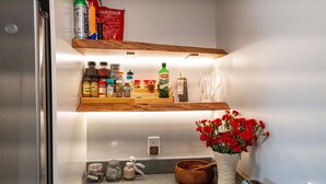 Una cocina con estantes de madera, un tostador, un florero con flores rojas y varios utensilios de cocina.