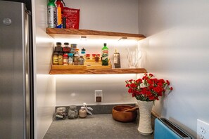 Uma cozinha com prateleiras de madeira, uma torradeira, um vaso com flores vermelhas e diversos utensílios de cozinha.