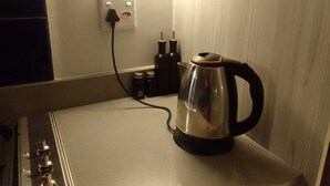 Une bouilloire en acier inoxydable posée sur un comptoir blanc, avec une prise de courant et deux bouteilles en arrière-plan.