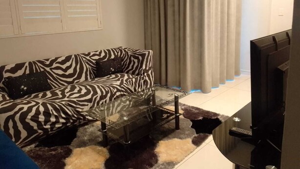Un salon avec un canapé à motifs zébrés, une table basse en verre, un téléviseur et un rideau.