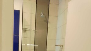 Une cabine de douche étroite, fermée par des parois de verre, dotée d’un pommeau de douche vertical, de murs recouverts de carreaux blancs et d’un mur d’accent bleu.