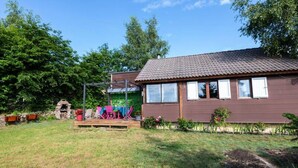 A single-story house with a tiled roof, a porch with chairs, and a small garden area. - G[?]aete de France 4 People (Antrenas)