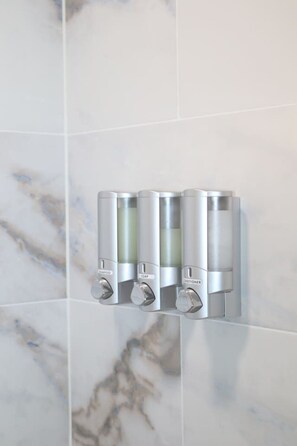 Un bagno con una parete in marmo e un dispenser di sapone a parete.