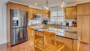 A modern kitchen with wooden cabinets, stainless steel appliances, and a central island with bar stools. - Canoe, Swim & Hike: Lakefront Brandenburg Home! (Brandenburg)