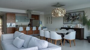 Eine moderne Küche mit weißen Schränken, ein Essbereich mit einem weißen Tisch und Stühlen sowie ein großes abstraktes Gemälde an der Wand.