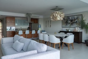 A modern kitchen with white cabinets, a dining area with a white table and chairs, and a large abstract painting on the wall. - Oceanfront Peninsula PtoVallarta/3BR• (Puerto Vallarta)