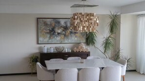Ein moderner Essbereich mit einem weißen Tisch, sechs Stühlen, einer dunklen Holzkommode und einem großen, abstrakten Gemälde an der Wand.
