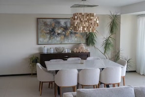 A modern dining room with a white table, six chairs, a dark wooden cabinet, and a large abstract painting on the wall. - Oceanfront Peninsula PtoVallarta/3BR• (Puerto Vallarta)