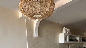 Ett kök med en böjd köksö, två flätade pallar, en hängande lampa och en inbyggd hylla med köksredskap.