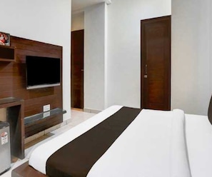 A hotel room with a bed, a television mounted on a wooden panel, a door, and a small table with a chair.