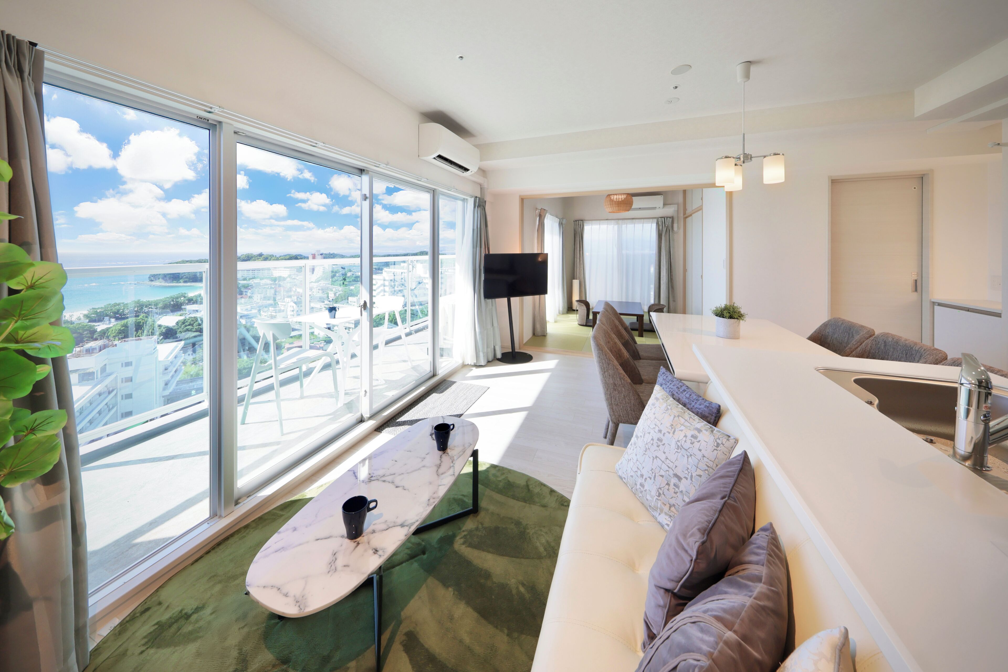 Una sala moderna con un ventanal grande, un sofá, una mesa de comedor y una zona de cocina.