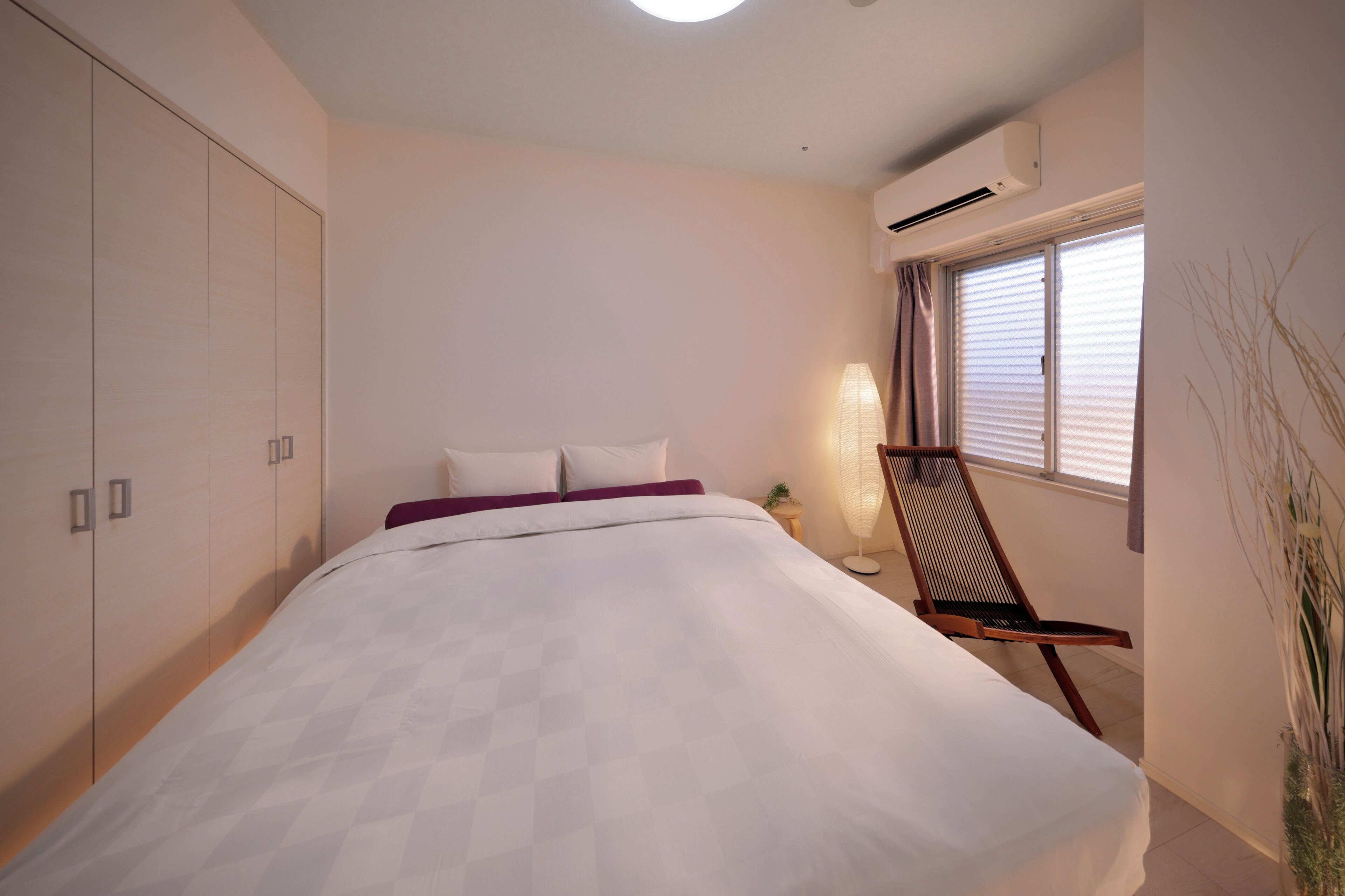 Un dormitorio con cama, una silla, aire acondicionado y ventana con persianas.