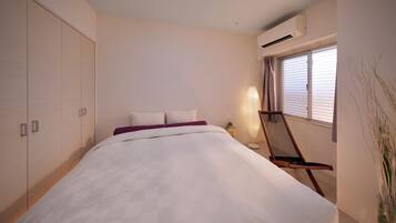A bedroom with a bed, a chair, an air conditioning unit, and a window with blinds.