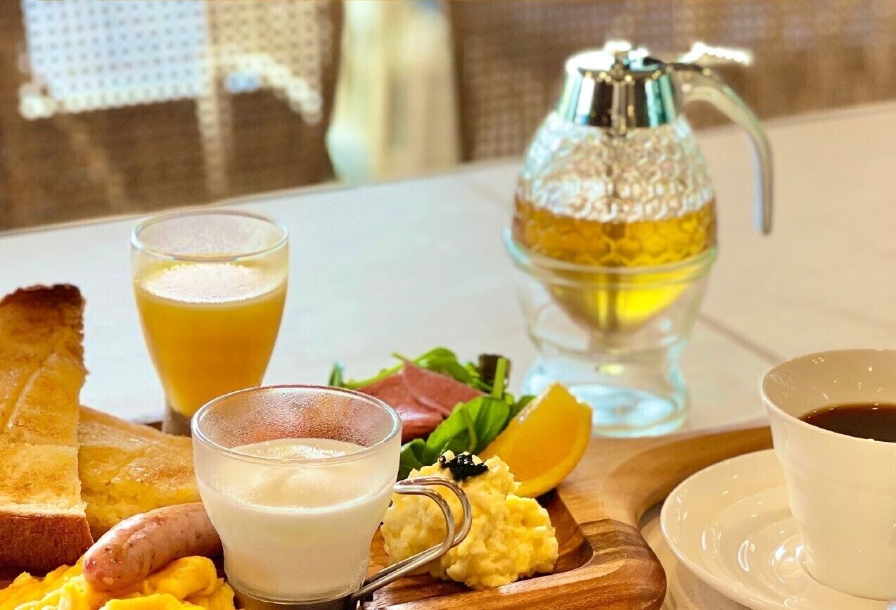 A breakfast setting with toast, scrambled eggs, sausage, a glass of orange juice, a glass of milk, a cup of coffee, and a bottle of honey.