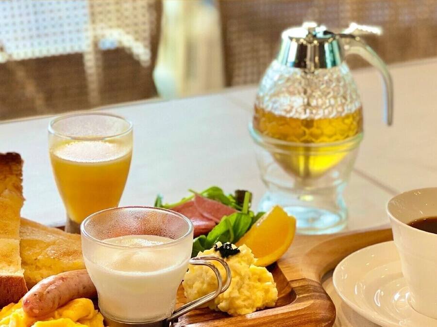 Una colazione con pane tostato, uova strapazzate, salsiccia, un bicchiere di succo d'arancia, un bicchiere di latte, una tazza di caffè e una bottiglia di miele.