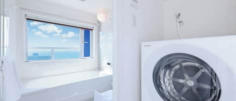 A modern bathroom with a bathtub, a window with a city view, and a white washing machine.