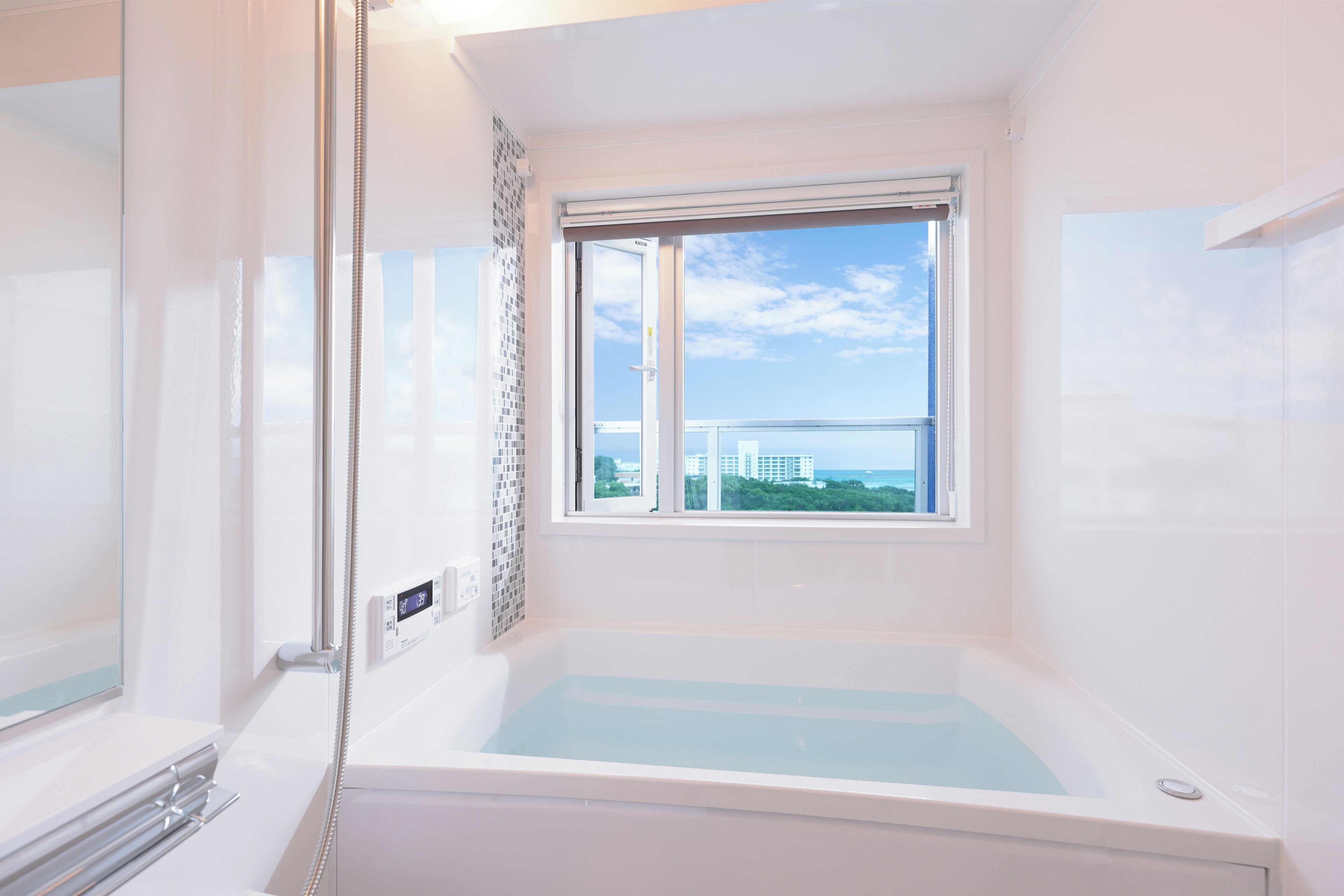 A bathroom with a bathtub, a shower, a window with a view of buildings, and a thermostat on the wall.