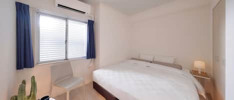 A modern bedroom with a large bed, a chair, a small table with a cactus, and a window with curtains.