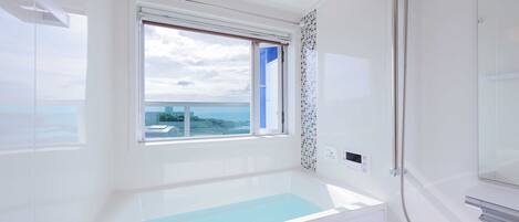 A modern bathroom with a bathtub, a shower, and a window with a view of the sea.