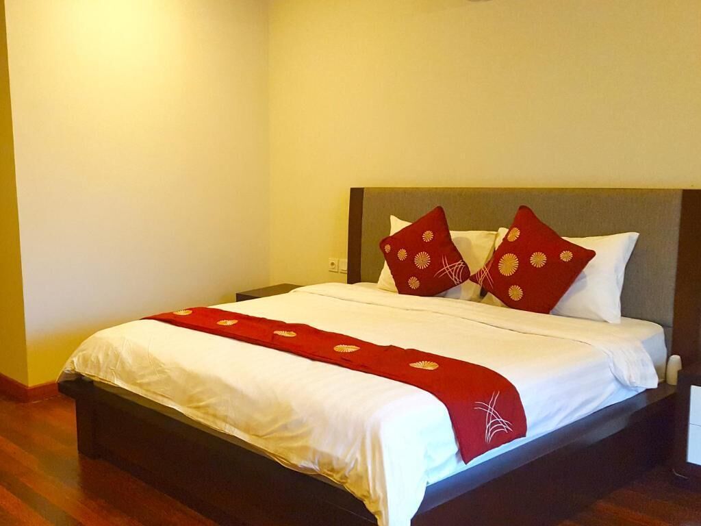 Una cama bien hecha con ropa blanca y almohadas rojas, una manta roja y un cabecero de madera.