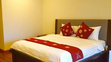 Una cama bien hecha con ropa blanca y almohadas rojas, una manta roja y un cabecero de madera.