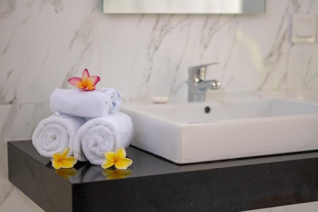 Un baño con pared de mármol, un lavabo blanco y toallas con motivos florales.