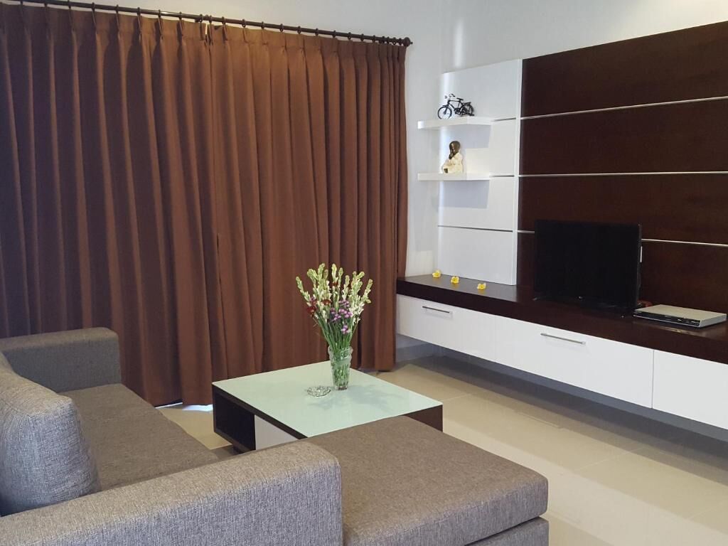 Un salon moderne comprenant un canapé, une table basse ornée d’un vase de fleurs, un téléviseur à écran plat et un meuble de rangement blanc doté d’étagères.