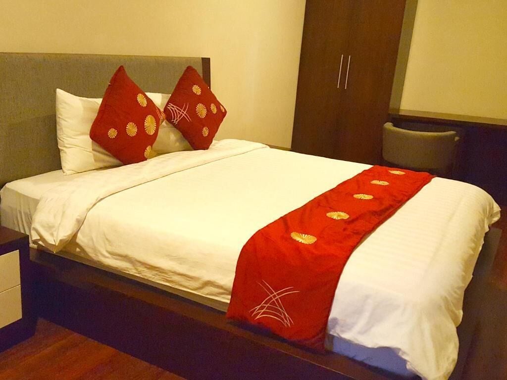 Een hotelkamer met een bed, nachtkastje, kledingkast en een stoel.