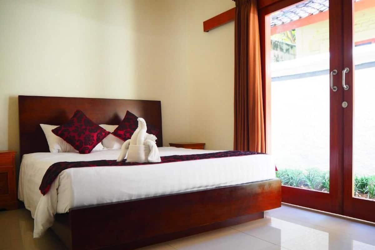 A neatly made bed with a wooden headboard, white bedding, and red patterned pillows.