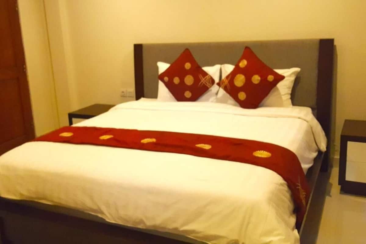 A neatly made bed with white linens and a red blanket, two pillows with a red and gold pattern, and a dark headboard.