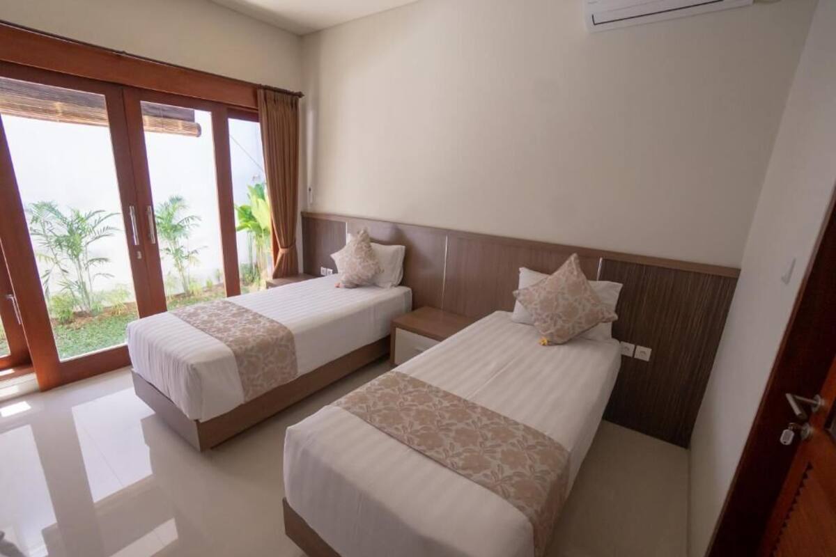 A hotel room with two beds, a sliding glass door to a garden, and a ceiling fan.