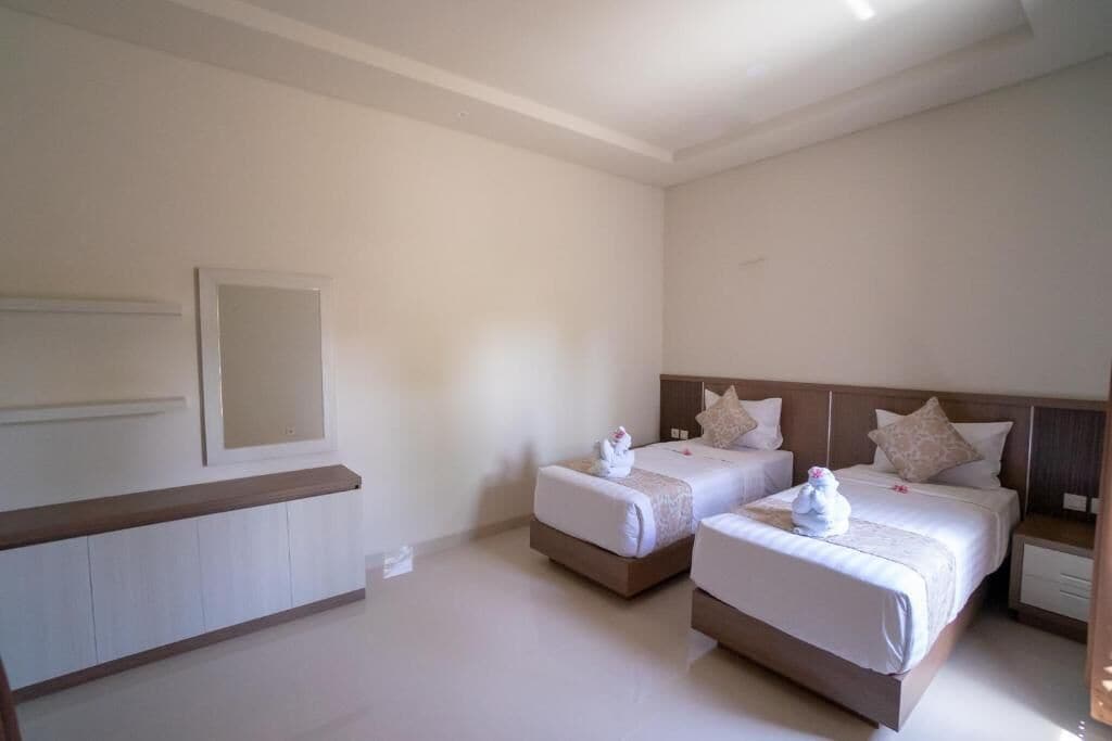 A hotel room with two beds, a wooden bench, and a large mirror on the wall.