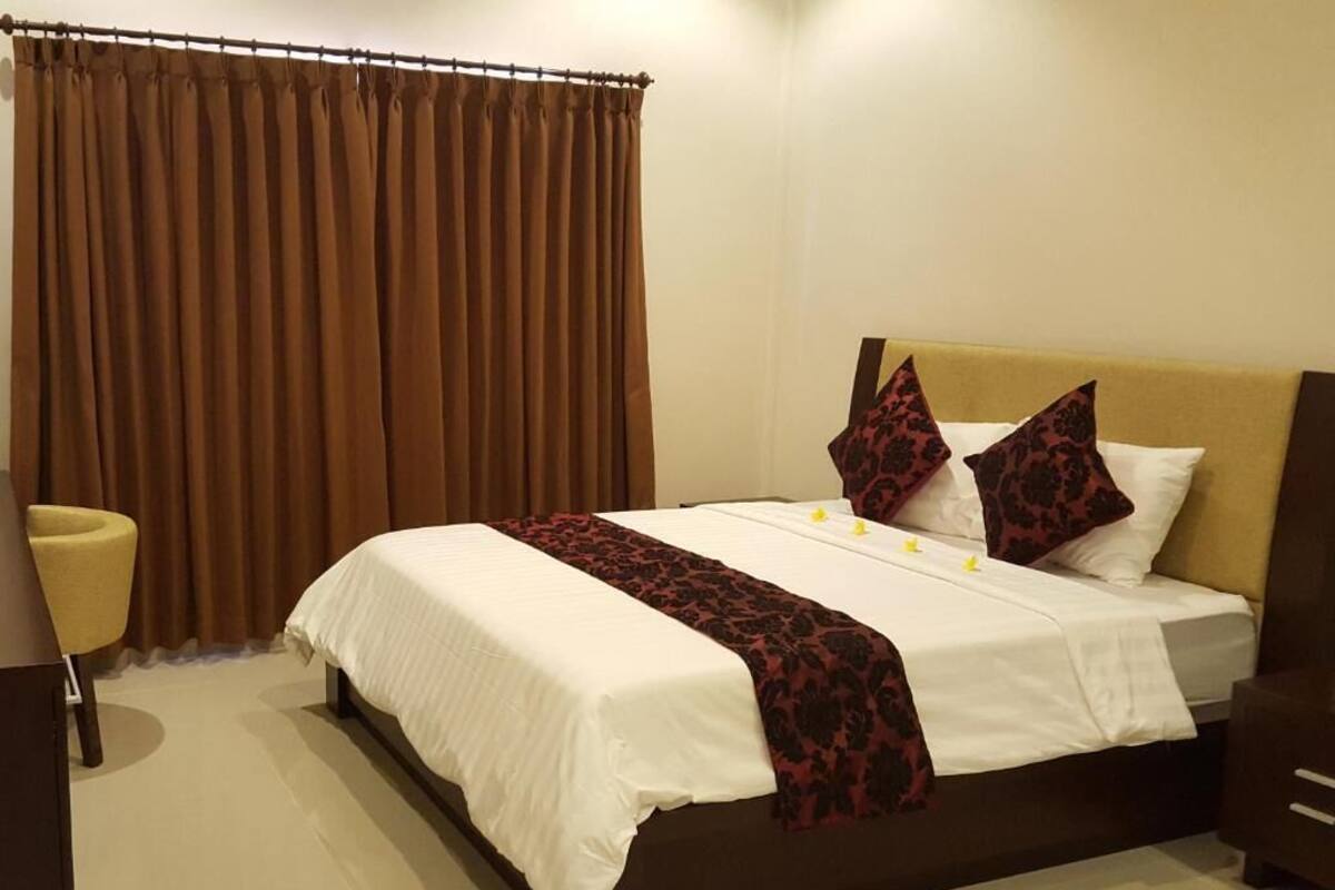 A neatly made bed with white linens and a dark red patterned throw, a headboard, and two decorative pillows.