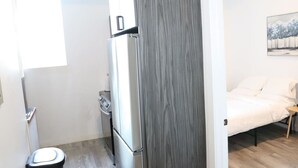 A compact room with a kitchenette, a bed, and a painting on the wall. - Budget 1BR for 2 Guests in Pavonia (Jersey City)