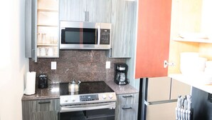 A compact kitchen with a microwave, stove, coffee maker, and a cabinet with kitchenware. - Budget 1BR for 2 Guests in Pavonia (Jersey City)