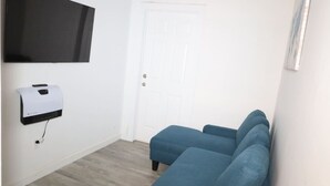 A room with a blue sofa, a mounted air conditioning unit, a white door, and a wall-mounted television. - Budget 1BR for 2 Guests in Pavonia (Jersey City)